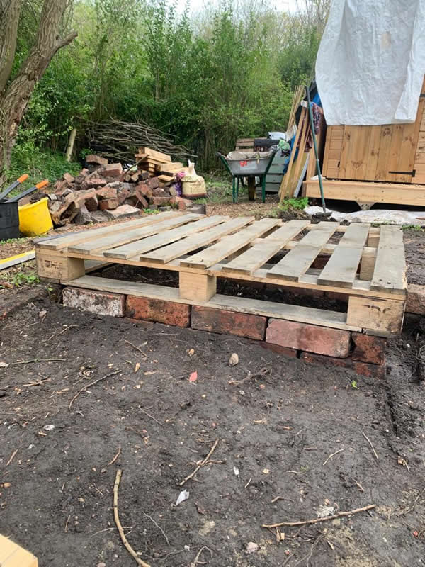 The brick foundations and pallets in place for the raised bed pallet collars